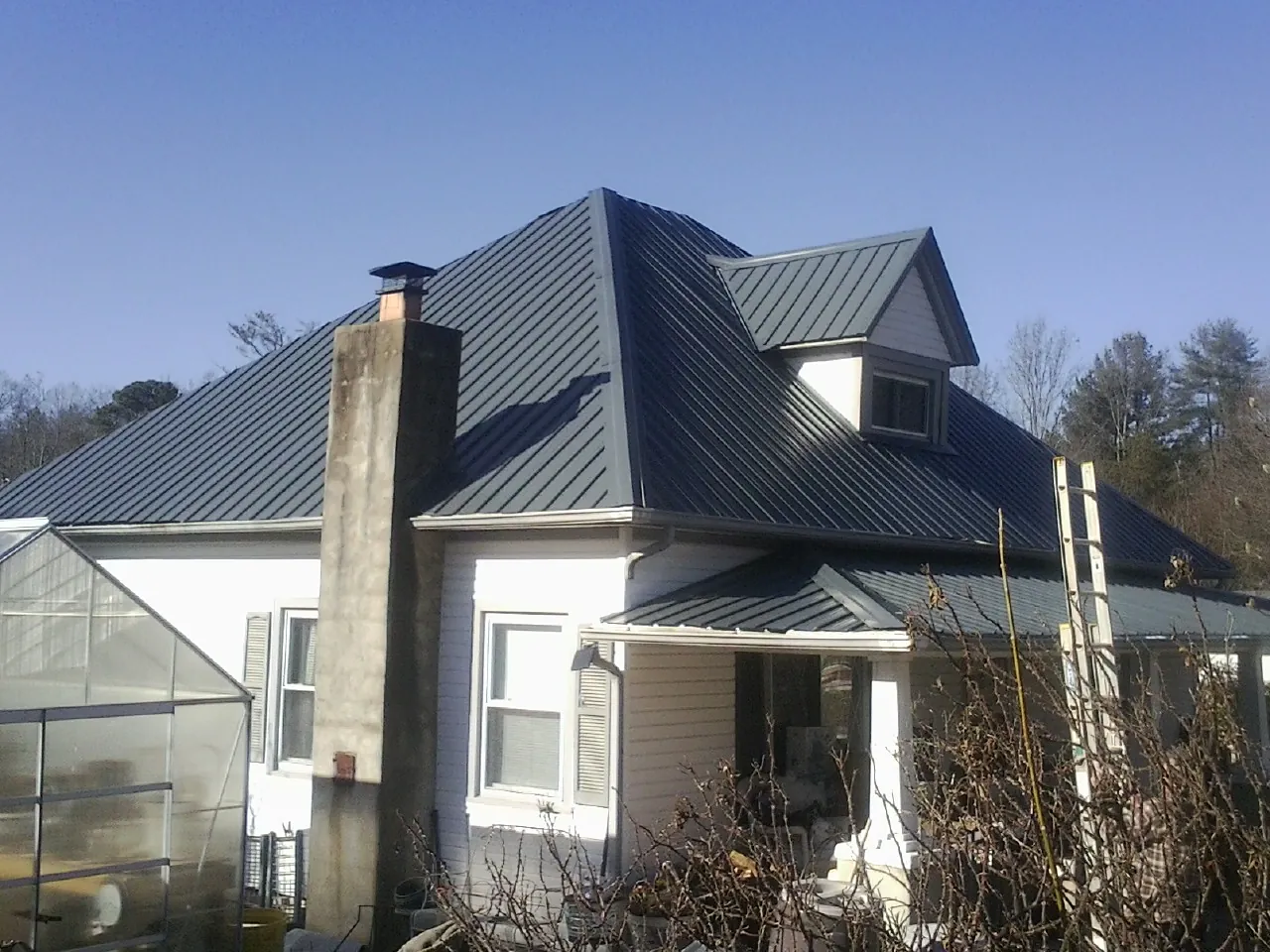 Dark blue standing seam metal roof on a white farmhouse with dormer — Slate & Tile Roof Repair by Roofing Brothers in Dyer