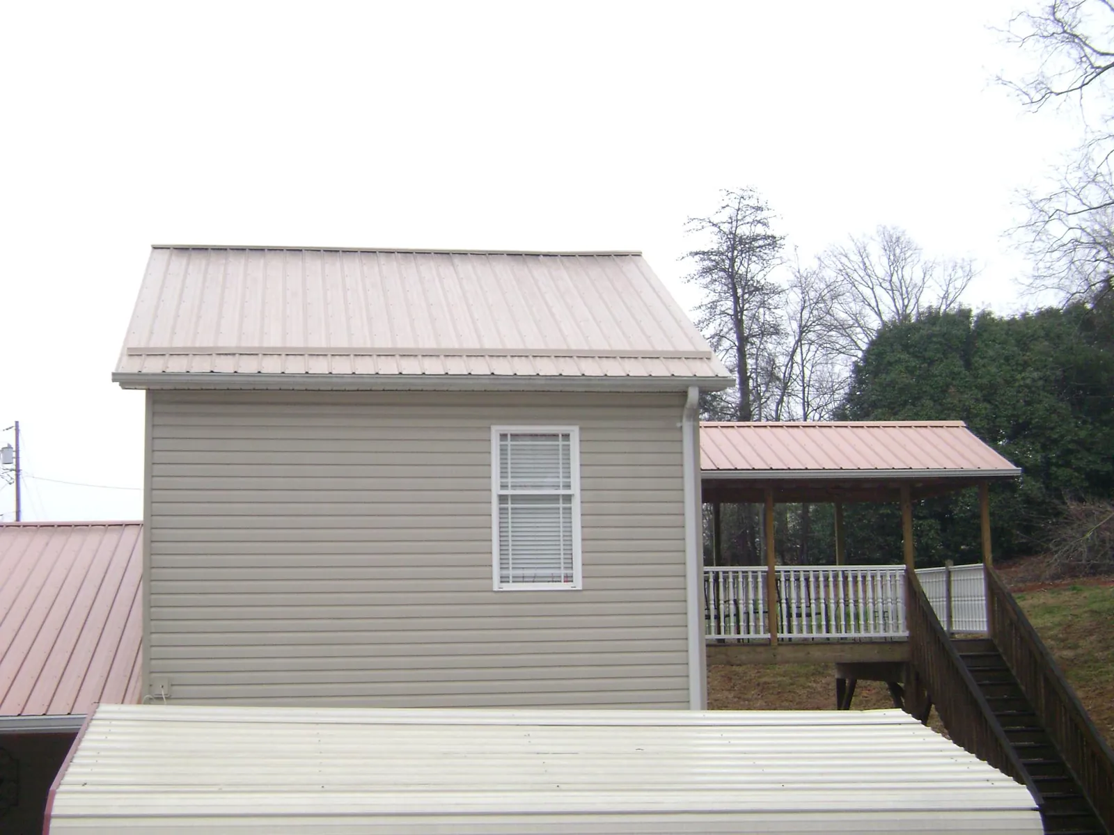 Tan metal roofs on a two story addition and attached porch, from a Roof Replacement job in Dyer